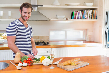 Man slicing fresh vegetables on cutting board at kitchen island with wine glass, copy space