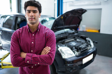 Asian male mechanic examining exposed engine under lifted car in service bay with roller door