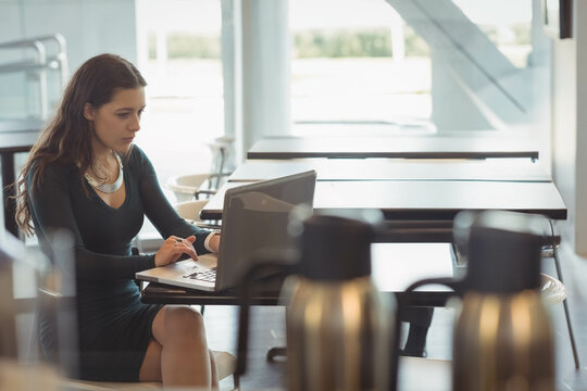 Woman in twenties working on laptop at modern cafe with pen and coffee urns, copy space