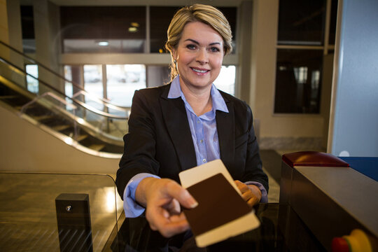 Female airline staff smiling and extending passport at glass check-in desk with scanner