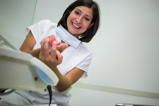 Female dentist smiling while holding pink dental mold and wearing surgical mask at clinic exam room
