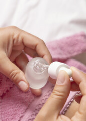 Closeup of young woman in pink bathrobe opening dropper bottle top view, cosmetic mockup