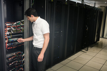Technician plugging multicolored ethernet cable into switch in data center aisle with server racks