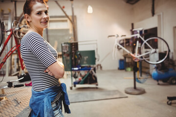 Female bicycle mechanic standing inside repair shop near metal workbench and white bike, copy space