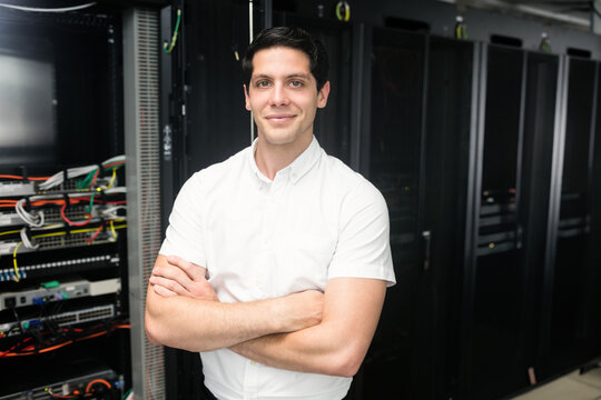 Man standing arms crossed, monitoring network switches and servers with patch cables in server room