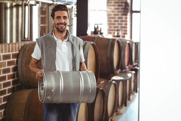 Man holding steel keg while standing inside brewery cellar with barrels and fermentation tanks