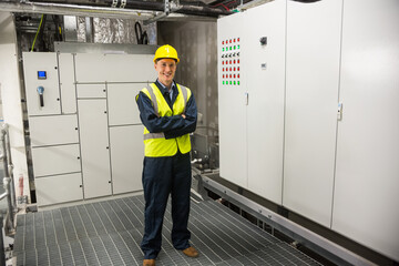 Male technician wearing hard hat standing in equipment room by control panel and indicator lights