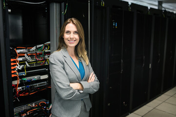 Female IT professional wearing suit jacket standing between server racks inspecting network cables