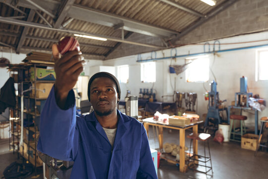 African American man in work coat inspecting circular metal component in workshop with machinery