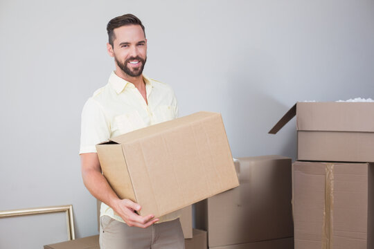 Man carrying cardboard box while unpacking moving supplies in sparse room, copy space