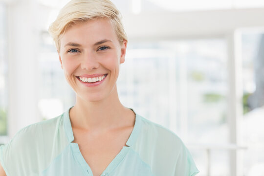 Woman in her twenties wearing mint blouse smiling at camera in large windowed room showing greenery