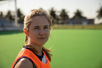 Female athlete standing on turf field wearing orange mesh bib and hoop earrings near white goalpost
