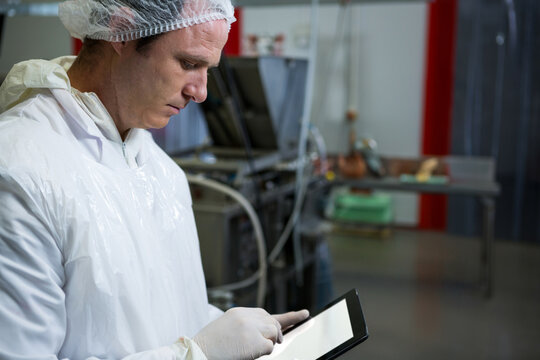 Mid adult man wearing protective gown and hair net holding tablet in processing plant, copy space