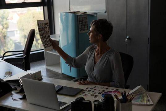 Contact sheets being examined against window light on white desk with laptop and camera