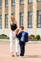 Fototapeta premium A first-grader boy gives autumn flowers to a teacher on 1st September in the school yard. Tradition to give flowers to the teacher on the first day of school. Knowledge Day. Teacher's Day