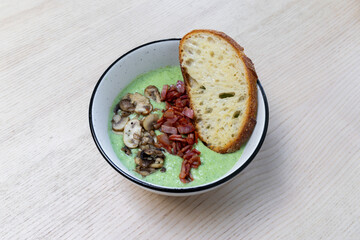 A bowl of broccoli soup with bacon, mushroom, and bread.