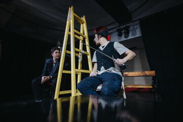 Two young performers engage in an intense theater rehearsal, utilizing creative props like a...