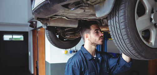 Male mechanic inspecting vehicle underside on hydraulic lift near wheel well in repair workshop