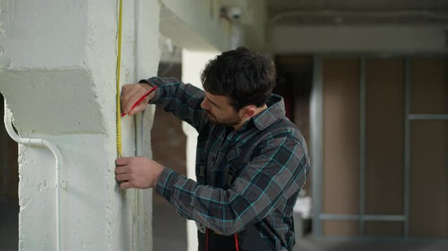Caucasian man architect builder measure wall using tape ruler measuring tool building renovation repairman guy male foreman handyman engineer inspect construction measurement equipment meter precision