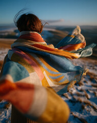 Woman in Colorful Scarf on Snowy Mountaintop at Sunset