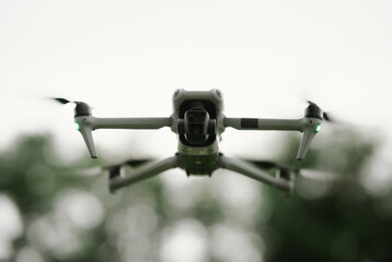 A gray drone with green lights hovers mid-air, indicating its active flight for surveillance or photography.