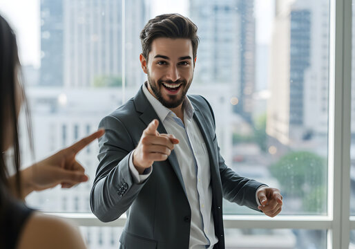 Happy businessman points playfully at viewer, colleague points back, modern office background.