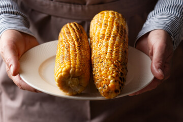 Caucasian male hands holds plate with grilled sweetcorn