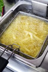 French fries cooking in boiling oil inside deep fryer