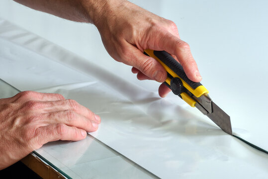 Hands cutting material with yellow box cutter knife on flat surface