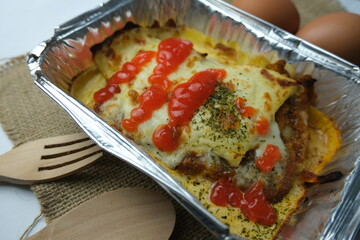 Baked lasagna served in an aluminum foil container, topped with melted cheese, tomato sauce, and sprinkled herbs.