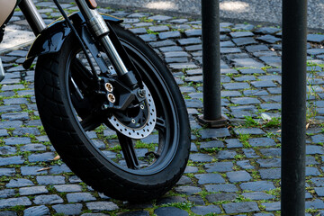 Motorcycle wheel with a disc brake on a cobblestone pavement.