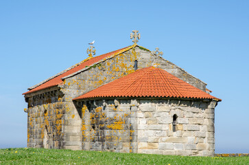 Historic stone chapel with traditional red roof sits on grassy hill, featuring ornate crosses and...