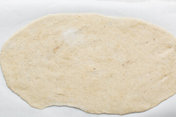 Overhead view of rolled out crackers dough on parchment paper, cracker biscuit dough on white background, process of making crackers