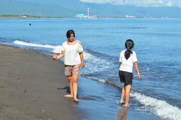 Two teenage girls stand peacefully, gazing at the ocean while soaking in the fresh air. The waves...