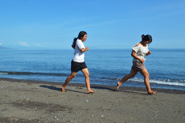 Fototapeta premium Two teenage girls run freely along the sandy beach, letting the ocean breeze guide them as they soak up the peaceful yet lively atmosphere of the bright morning waves.