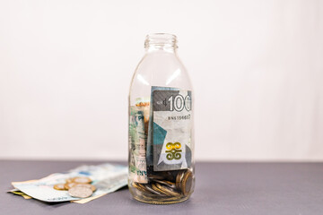 Minimalist Savings Jar with Ghanaian Cedi Banknotes and Coins. Concept of personal finance, saving money, frugality, building wealth over time, and creating an emergency fund.