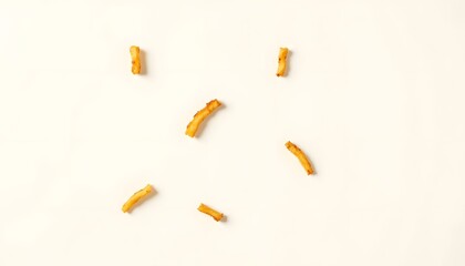 A stark white backdrop showcases a scattering of golden brown fried potato strips, each cut uniformly, arranged artfully with subtle variation in direction