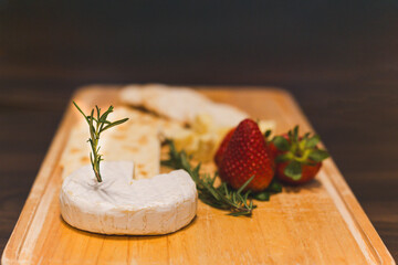Seleted focau on pieces of cheese with strawberry and cracker on wooden board.
