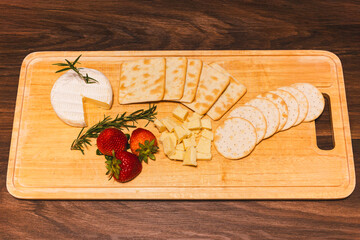 Appetizer different types of cheeses on cutting board with fresh strawberries on wooden table.