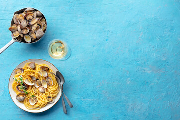 Vongole clams with spaghetti pasta, with white wine, overhead flat lay shot. Seafood linguine on a blue background with copy space