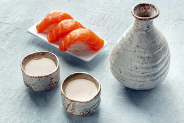 Sake in a pitcher and ochoko, traditional cups, with salmon nigiri, traditional Japanese food and drink. Ceramic set