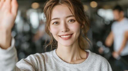 Happy young woman waving at the camera in a bright gym setting, showcasing fitness and positivity in a vibrant workout environment