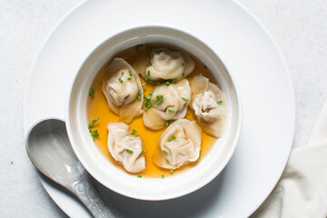 Overhead view of wonton soup in a white ceramic bowl, clear soup with dumplings in a white soup bowl