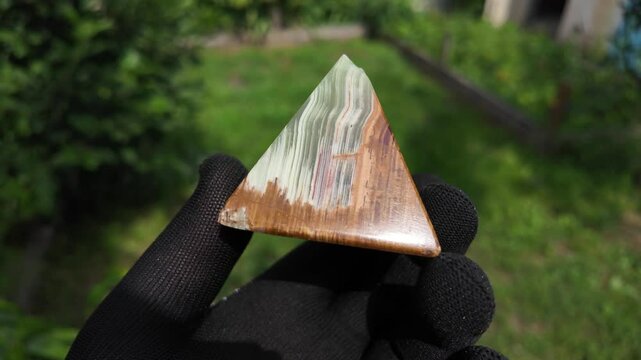 Middle-aged woman with green orgone stone pyramid. triangular stone pyramid. pyramid on the palm. stone symbol. magic item. Man showing a green orgone pyramid, close up