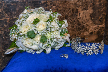 Wedding bouquet with white roses and baby's breath placed beside a silver tiara and two engagement...
