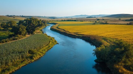A calm river winds through lush green and golden fields under a clear blue sky, showcasing a serene rural landscape.