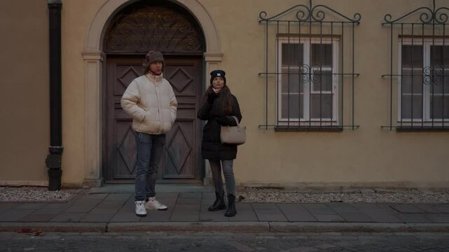 Young man has walked his girlfriend home after their date. Standing at her doorstep in the evening, they linger, reluctant to say goodbye, making small talk about his route home to prolong the moment.