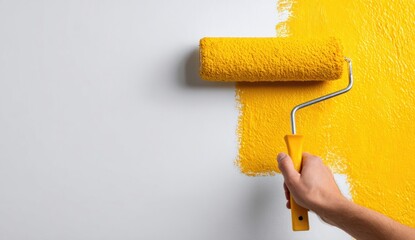 Arm painting wall with yellow roller contrasting freshly painted area with blank space