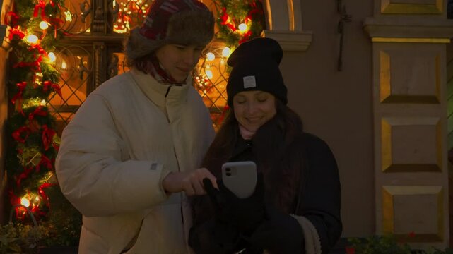 A young couple reviews and chooses photos on a smartphone right after taking a Christmas selfie. They smile and point at the screen, happily reliving the moment from their romantic evening date.
