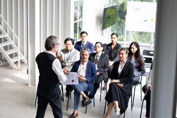 Fototapeta premium Back view speaking training in seminar : Senior caucasian business man leader in seminar, speaking on business training with group of diverse people company employees in meeting room
